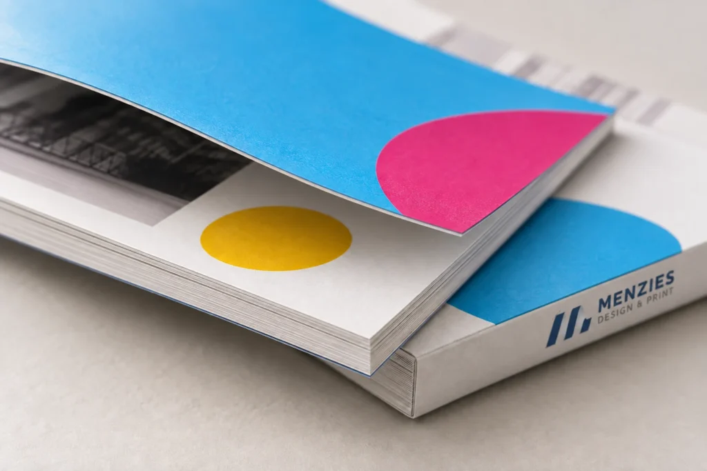 Illustrative close-up of a cyan brochure cover, paper layers and a square-bound spine.